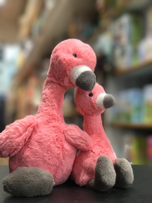 2 stuffed animal flamingos sitting next to each other on a shelf in a toy store.